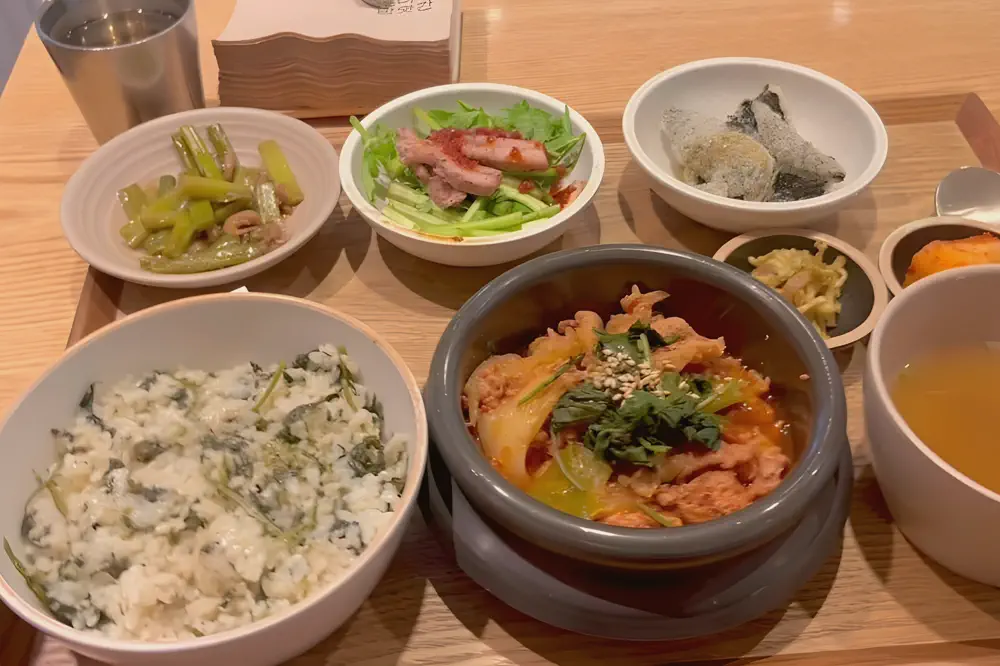 食堂のトレーに並ぶ韓国の定食一膳（ごはん、チゲ、スープと小鉢）